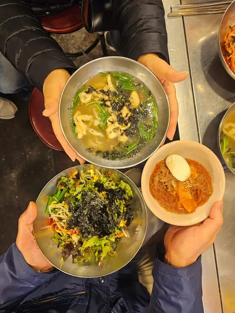 Twelve Korean dishes lined up at a historic Gwangjang market kitchen on a seoul food tours lunchtime tasting in Seoul, South Korea