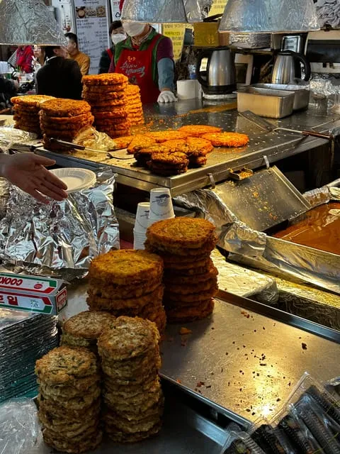 Local chef plating bindaetteok at a stall in historic Gwangjang Market on a seoul food tours chef-led tasting in Seoul, South Korea